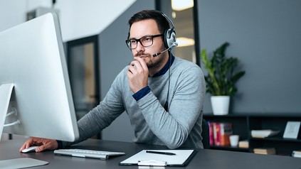 Mann sitzt mit einem Headset vor dem Computer