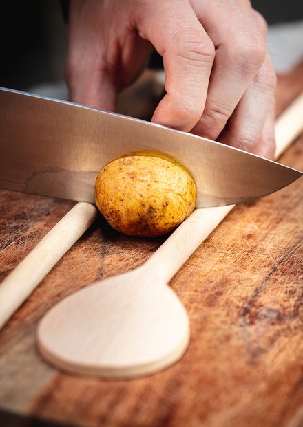 Um die Fächerkartoffeln einfach zuzubereiten, werden die ungeschälten rohen Knollen jeweils zwischen zwei Holzlöffel gelegt.