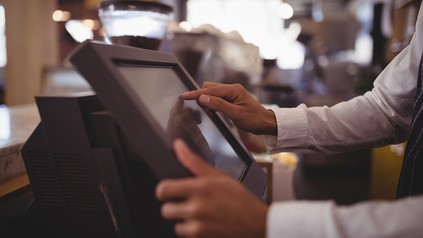 Nahaufnahme eines jungen Kellners, der etwas in einen Touchscreen-Monitor der Kasse eintippt