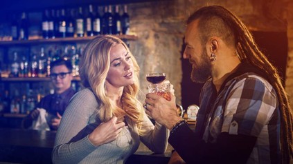 Eine junge Frau spricht an der Bar mit einem Mann, im Hintergrund beobachtet der Barkeeper das Geschehen