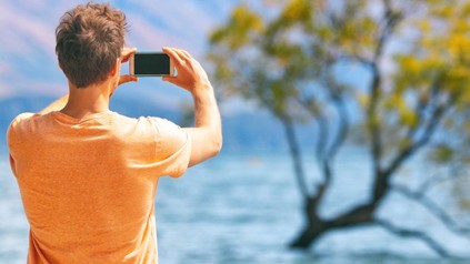 Mann fotografiert Baum in einem See mit dem Handy