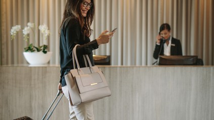 Frau an der Hotelrezeption mit Handy in der Hand