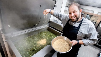 Nico Winkelmann, Koch und Geschäftsführer im "Bümmersteder Krug", bereitet in der Küche des Restaurants Grünkohl zu und gibt dabei die Zutat Grütze hinzu. (Foto: © picture alliance/dpa | Hauke-Christian Dittrich)