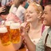 Junge Leute stoßen mit ihren Maßkrügen im Bierzelt auf der Wiesn an.