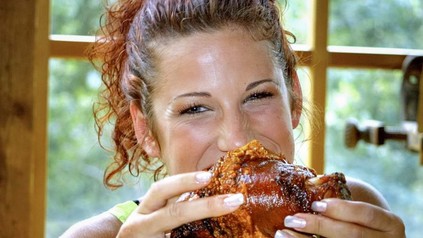 Eine hübsche Frau beißt genüsslich in eine Schweinshaxe