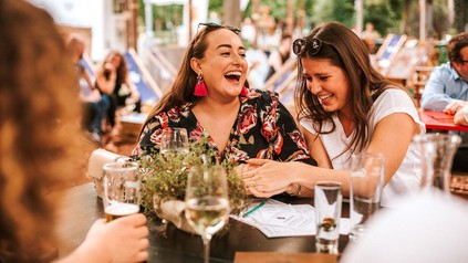 Zwei Frauen lachen bei einem Wein im Feuerdorf am Wiener Prater.