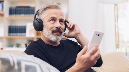 Älterer Mann hört auf seinem Handy einen Podcast