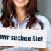 Eine Frau hält ein Schild vor sich auf dem "Wir suchen Sie" steht