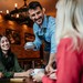 Mann bedient drei junge Frauen an einem Tisch in einem Cafe