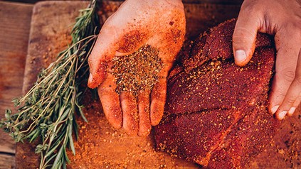 Eine Person würzt ein großes Stück Fleisch