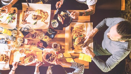 Mehrere Menschen sitzen an einem gedeckten Tisch und essen zusammen Burger