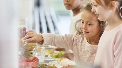 Drei Kinder nehmen sich Essen von einem Büfett in der Cafeteria