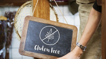 Nahaufnahme einer Frau mit Schürze, die eine Tafel mit der Aufschrift "Gluten Free" aufhängt; glutenfreie Ernährung