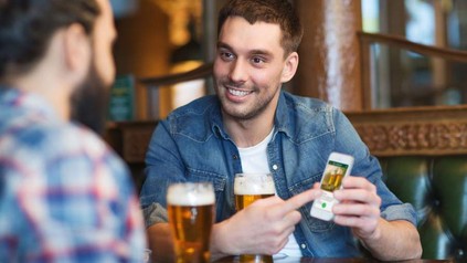 Ein junger Mann, der an einem Tisch sitzt und seine Rechnung mit dem Smartphone und der barforce-App begleicht.