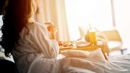 Eine Frau im Hotelzimmer schaut früh morgens aus dem Fester