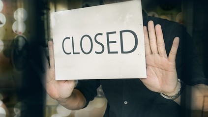 Ein Mann bringt ein "Closed"-Schild an die Glastür seines Restuarants an