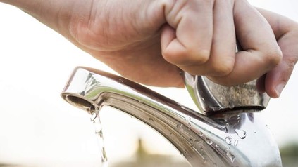 Mann dreht Wasserhahn zu